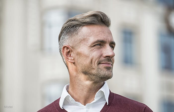 male model facing sideways wearing a marooon sweater on top of a neck shirt for tension free facelift