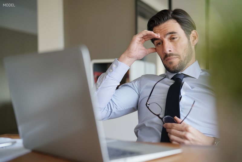 Tired, haggard businessman sitting in front of a laptop