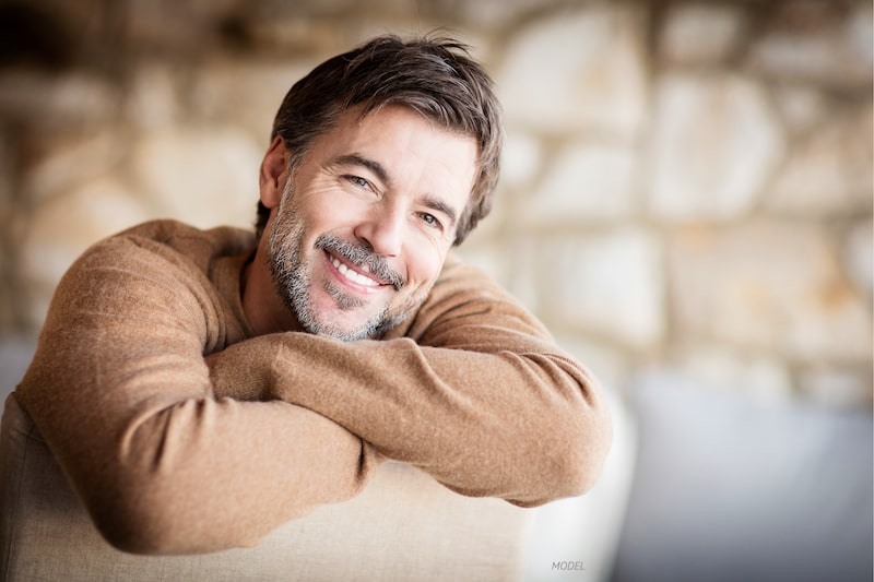 Middle-aged man with short beard leaning over the top of a chair, smiling.