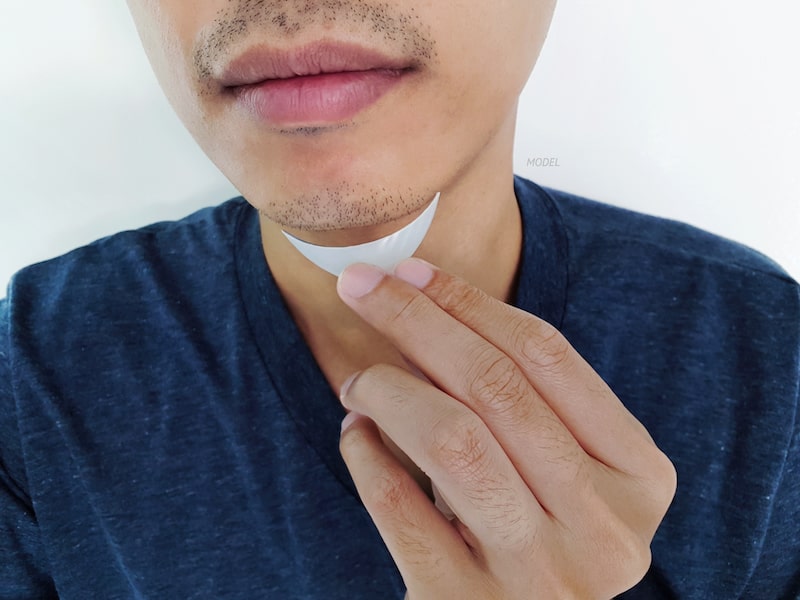 Young, Asian man holding a chin implant up to his chin.
