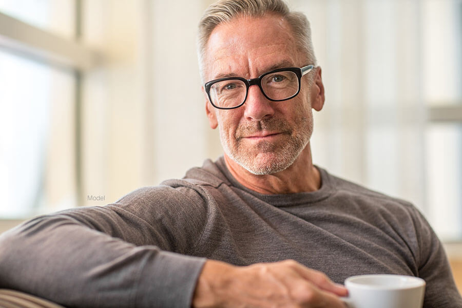 Attractive older man with chiseled jaw and natural features drinks coffee.