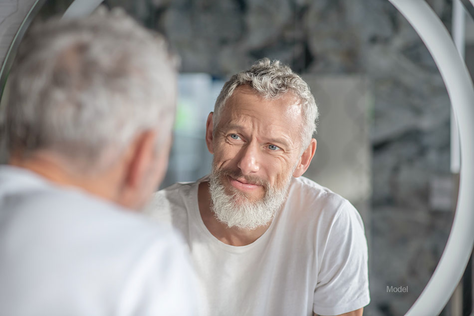 Middle aged man with a beard looks critically in a mirror